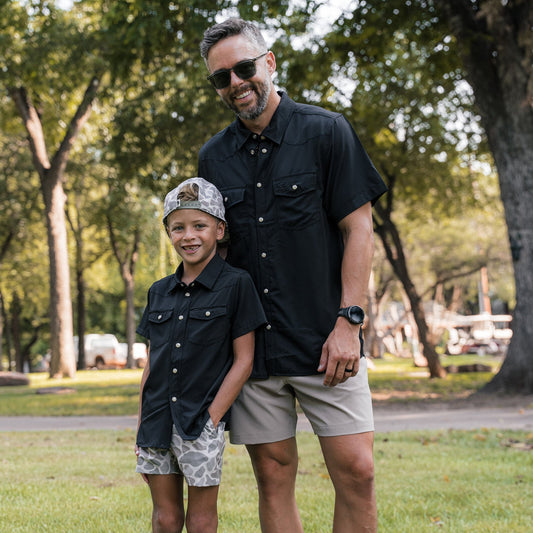 Man and young boy standing together in a park with trees in the background