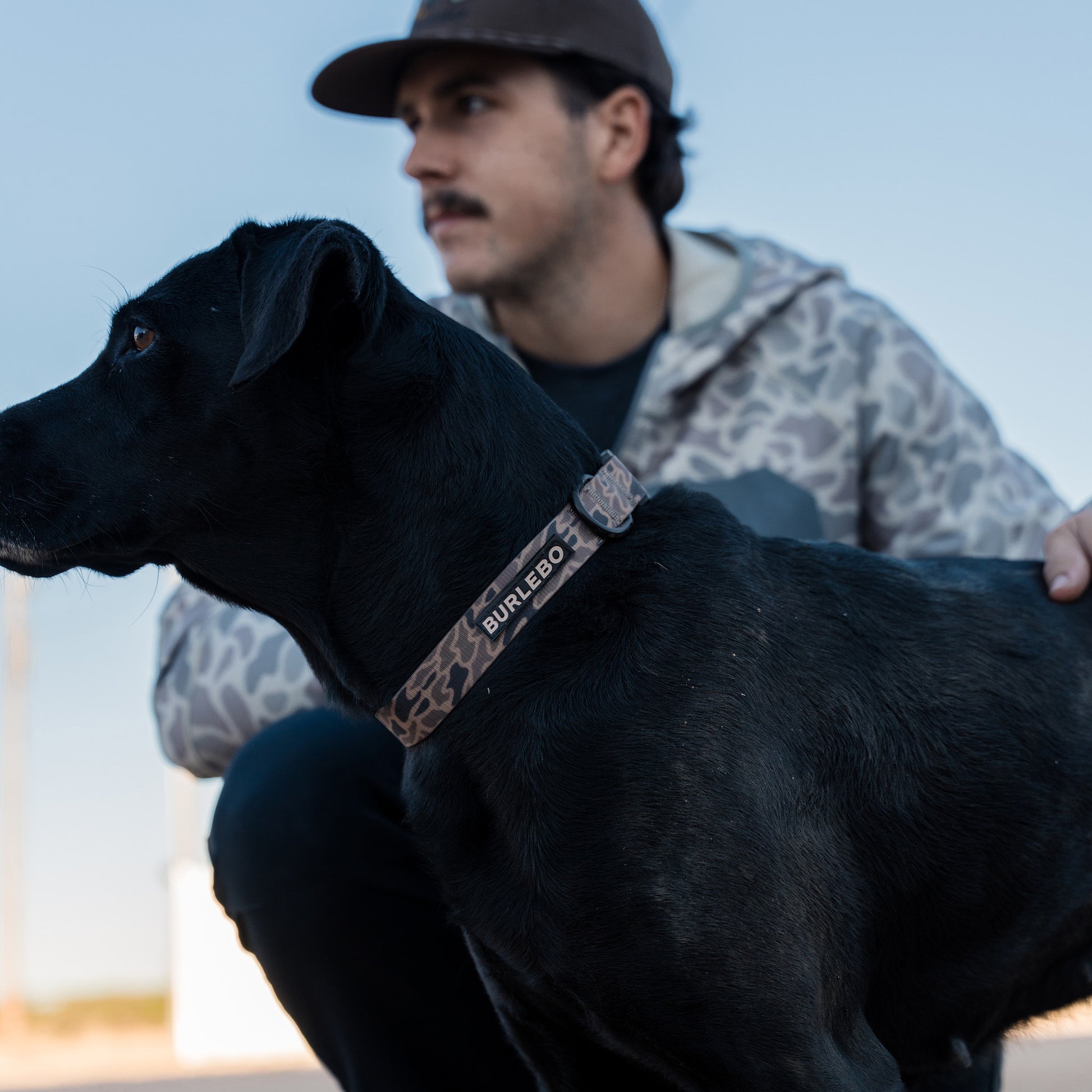 Man with a black dog wearing a leopard print collar outdoors