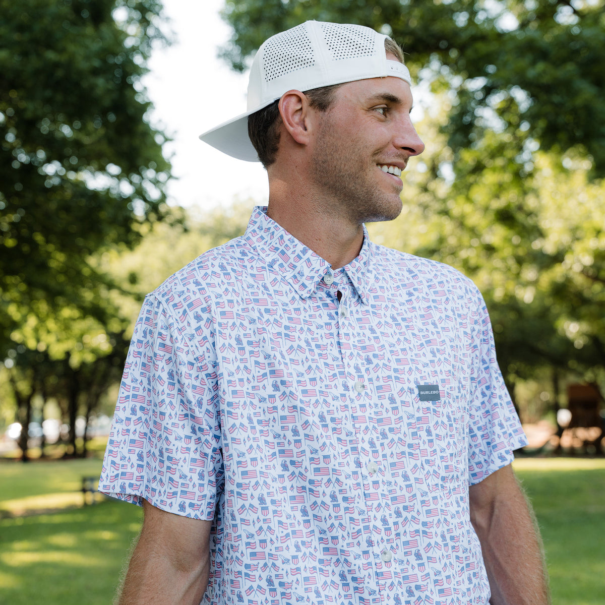 Man wearing a patterned shirt and white cap in a park setting