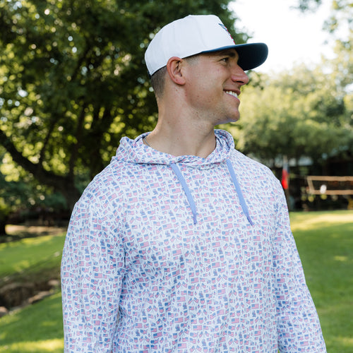 Man wearing a patterned hoodie and cap outdoors with trees in the background