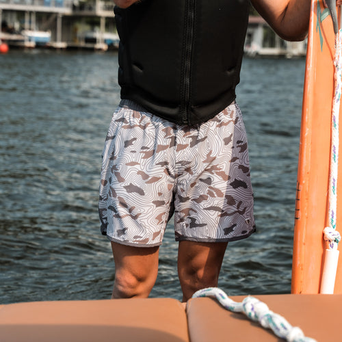 Person wearing patterned shorts standing on a boat with water in the background