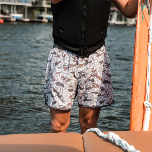 Person wearing patterned shorts standing on a boat with water in the background