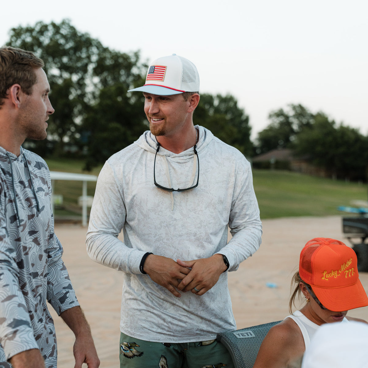 Two men and a child standing outdoors, with one man wearing a cap with an American flag design.