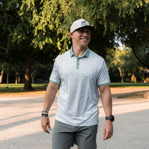 Man wearing a light gray polo shirt with green accents and a cap, standing outdoors.