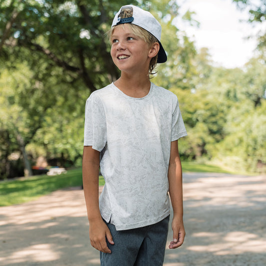 Young boy wearing a white t-shirt and cap outdoors with trees in the background