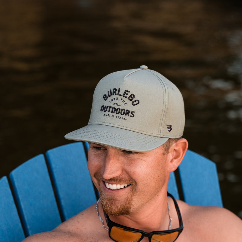Man wearing a cap with 'Burlebo' branding, sitting on a blue chair outdoors.