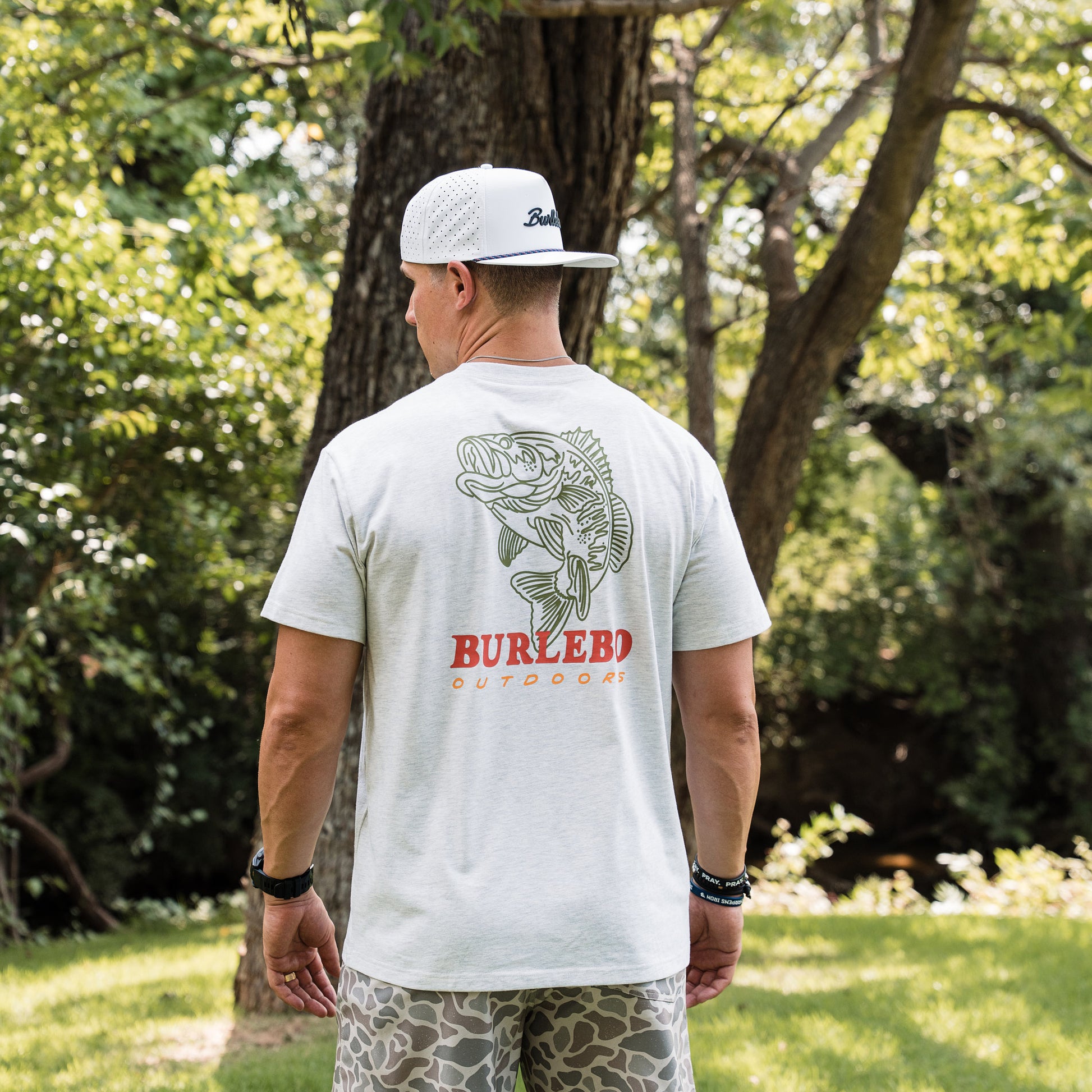 Man wearing a white t-shirt with a fish design and 'Burlebo Outdoors' branding, standing outdoors.