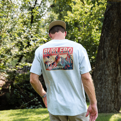 Man wearing a light gray t-shirt with 'Burlebo Outdoors' design outdoors.