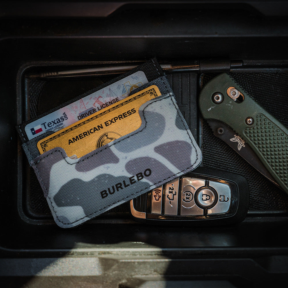 Camouflage cardholder with cards, key fob, and knife on a dark surface