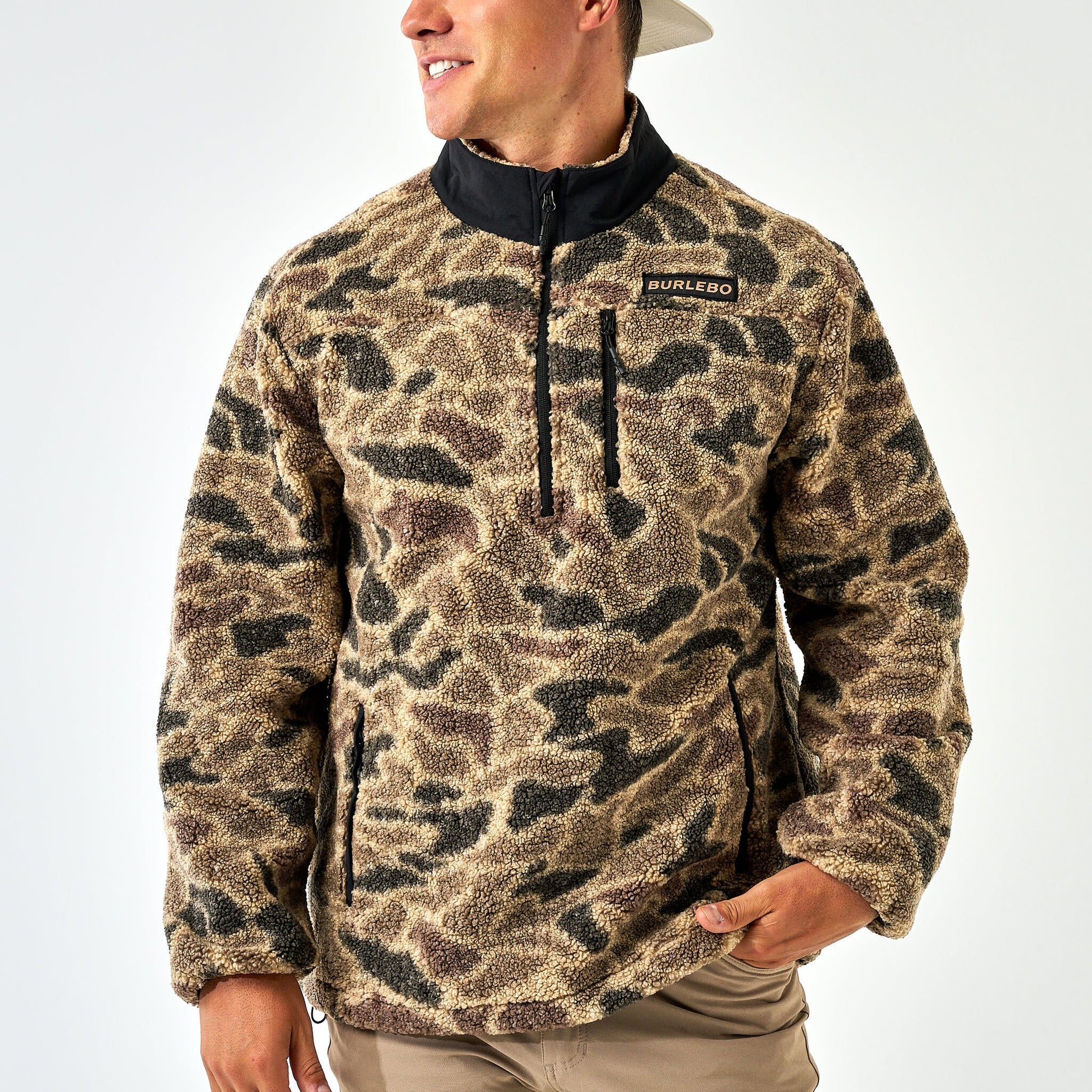 Person wearing a camouflage pullover with a visible brand logo on a white background