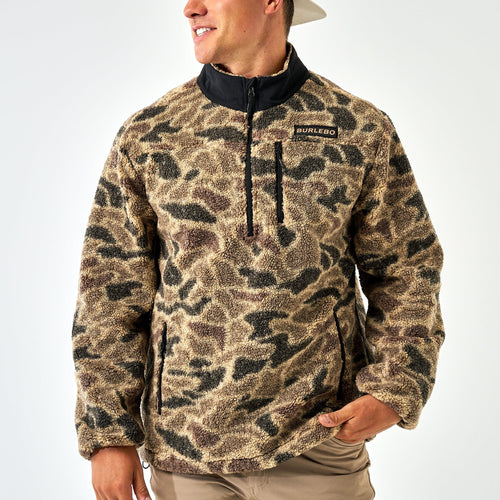 Person wearing a camouflage pullover with a visible brand logo on a white background
