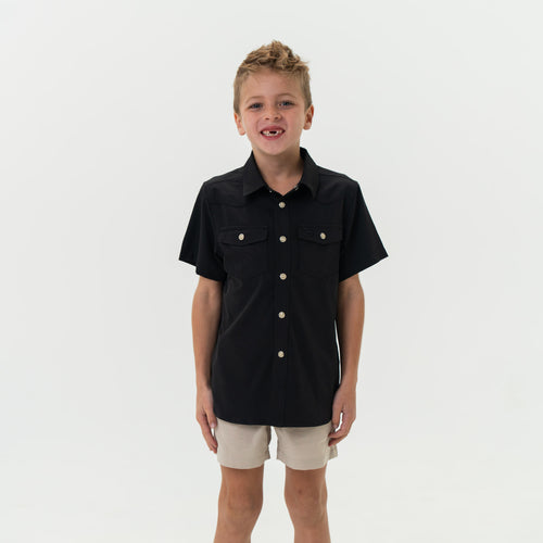 Child wearing a black short-sleeve shirt with buttons on a white background