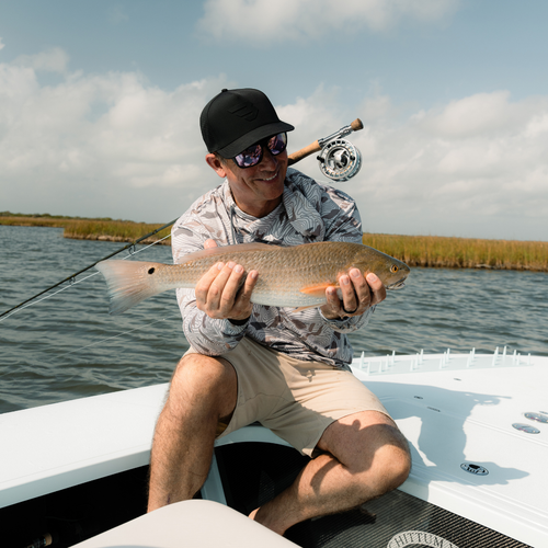 Man holding a fish on a boat with fishing rod and reel in the background