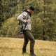 Hunter carrying a rifle across a meadow while wearing the Classic Deer Camo Challenger Jacket