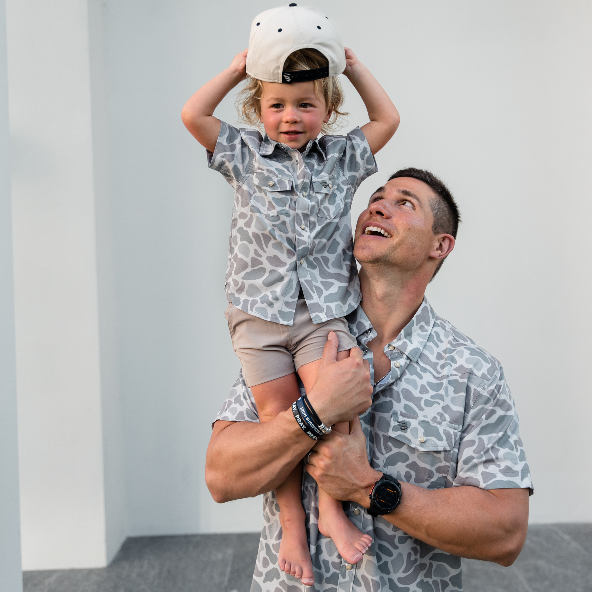 Man holding a child wearing matching patterned outfits against a plain background