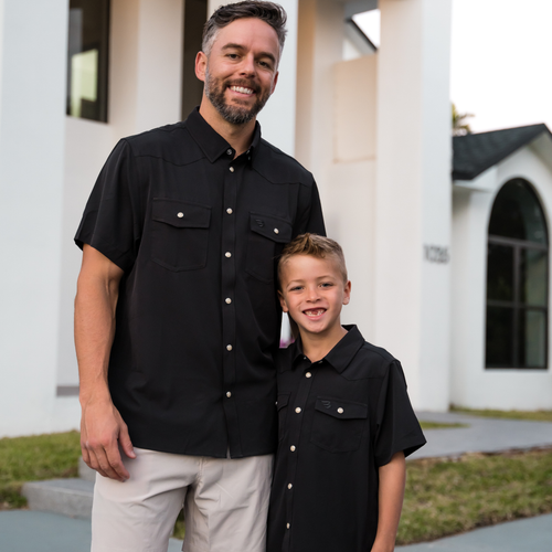 Man and young boy wearing matching black shirts standing in front of a building.