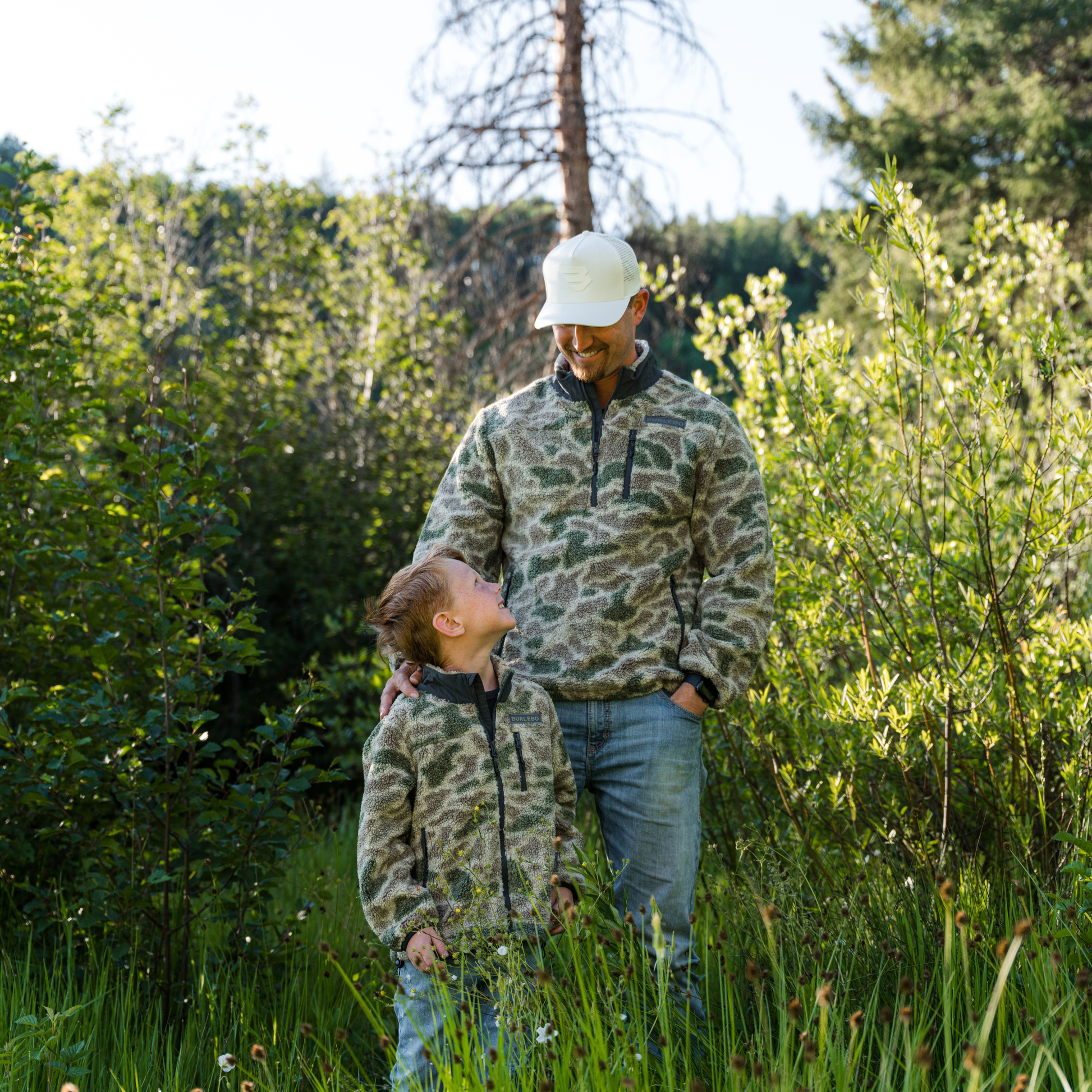 Man and child in matching camouflage outfits standing in a forest