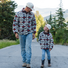 Man and child walking on a road with trees and mountains in the background