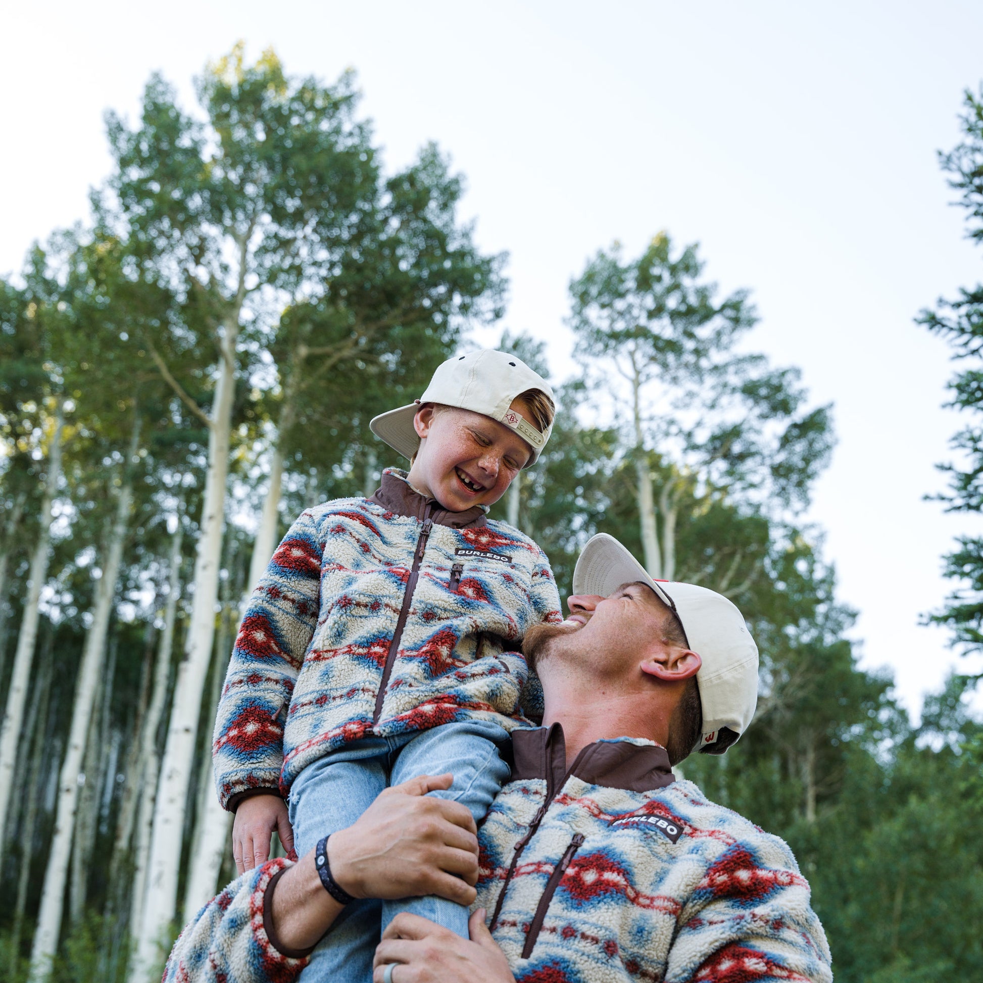 Man and child wearing matching patterned jackets and hats in a forest setting
